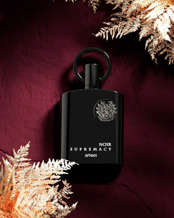 Black perfume bottle labeled 'Supremacy' on a dark background with decorative elements.