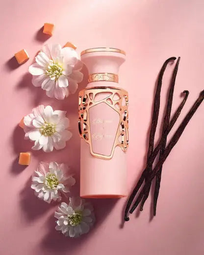 Pink perfume bottle with gold accents on a pink background with flowers and vanilla beans.